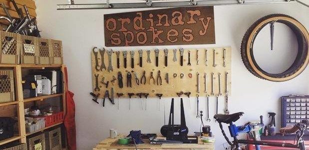 Sign that reads "Ordinary Spokes" above a workbench with bicycle tools.